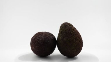 Beyaz bir masada iki avokado yatar. Avokadolar kahverengi ve olgun görünüyor. Avokado beyaz arkaplan üzerinde döner.