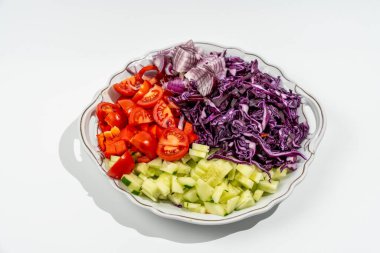 İçinde domates, salatalık ve lahana bulunan çeşitli sebzelerden oluşan beyaz bir tabak. Tabak, sebzelerin üst üste yığılmadan yayılacağı şekilde düzenlenmiş.