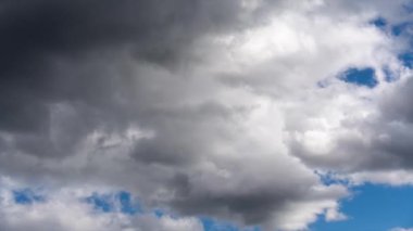 Siyah bulutların zaman akışı. Mavi gökyüzünde bulutlar süzülür dramatik bir atmosfer yaratır. Bulutlar karanlık ve ağırdır, fırtına izlenimi verir..