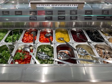 Farklı sebze ve meyvelerle dolu bir salata barı. Sebzeler farklı kaselerde ve meyveler ayrı bir kasede. Salata barı iyi organize edilmiş.