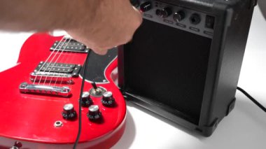 Gitarist enstrüman kablosunu gitar amplifikatörüne bağlıyor. Beyaz üzerine Gitar ve Yükseltici.