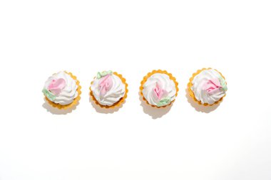 Pembe kremalı ve beyaz kremalı dört küçük kek. Şekerlemeler pembe çiçeklerle süslenmiş. Beyaz arkaplanda izole edilmiş tatlı.