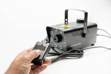 Bir kişi sis makinesinin yanında uzaktan kumanda tutuyor. Uzaktan kumanda siyah ve kırmızı ışığı var.