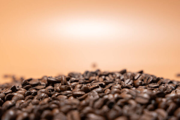 A pile of coffee beans on a table on a brown background. The beans are scattered and piled, creating a sense of depth and texture. The image evokes a feeling of warmth and comfort.