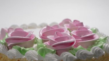 Üzerinde pembe krema ve yeşil yapraklar olan bir pasta. Pasta pembe güllerle süslenmiş. Dönen tatlı.