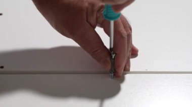 Adamın biri bir tornavida tutuyor ve bir dolap tahtasına vida sokmak üzere. Mobilya montaj konsepti.