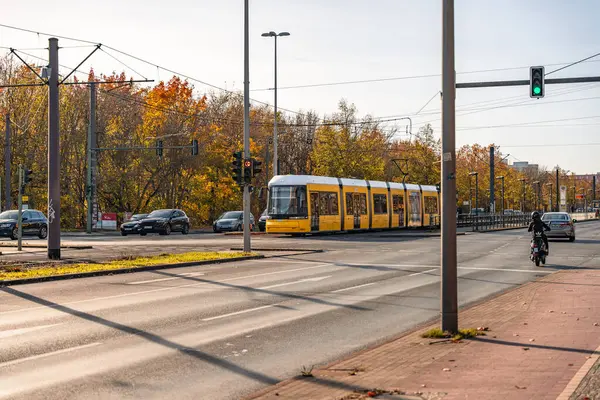 Almanya 3 Kasım 2024. Sarı ve beyaz bir tramvay cadde boyunca hareket ediyor. Tramvay arabalar ve motosikletlerle çevrilidir. Sokaklar trafik ışıkları ve arabalarla dolu.