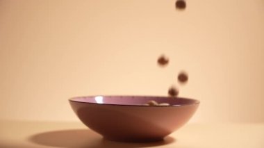 Çikolata taneleri turuncu arka planda bir fincana yavaş çekimde düşüyor. Turuncu arka planda bir fincanda çikolata taneleri..