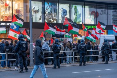 Almanya 16 Kasım 2024. Bir grup protestocu tarafından tutulan Filistin bayrakları polis çitin arkasında duruyor. Havada bir sürü bayrak var.