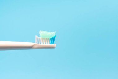 Üzerinde diş macunu olan bir diş fırçası mavi arka planda sergilenir. Diş macunu mavi ve beyazdır, ve diş fırçası beyazdır.