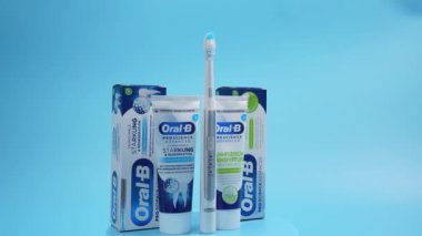 Oral B diş macunu ve diş fırçasıyla mavi ve beyaz kutu. Diş macunu bir tüpün içinde ve diş fırçası yanında duruyor. Diş macunu mavi arkaplanda döner.