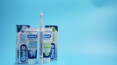 Mavi ve beyaz bir kutu Oral B diş macunu ve bir diş fırçası. Görüntü ürünü tanıtmak ve insanları diş macunlarını mavi arka planda kullanmaya teşvik etmek içindir..