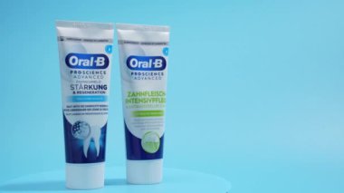İki tüp diş macunu, birinin adı Oral B. Mavi bir yüzey üzerinde tüpler yan yana diş macunu mavi bir arkaplanda döner..