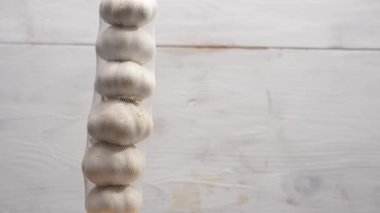 Bir ipten sarımsak soğanı sarkıyor. Ampuller beyaz ve sıra sıra dizilmiş. Sarımsak ahşap arka planda döner.