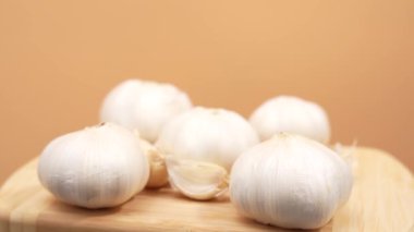 Tahta bir kesme tahtasının üzerinde bir demet sarımsak soğanı duruyor. Ampullerin hepsi farklı boyutlarda ve sıra sıra dizilmiş. Tazelik ve doğal güzellik kavramı. Sarımsak turuncu arka planda döner.