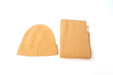 Beyaz arka planda sarı bir şapka ve bronz bir eşarp var. Şapka eşarbın sol tarafında, eşarp da sağ tarafında. Sıcaklık ve rahatlık kavramı