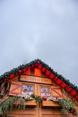 Kırmızı çatılı küçük tahta bir bina ve Gluhwein yazan bir tabela. Bina Noel süslemeleri ile süslenmiş ve rahat, şenlikli bir atmosferi var.