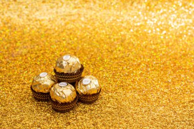 Ferrero Rocher chocolates in gold color sit on a gold background. The candies are arranged in a pyramid shape. The image has a warm tone