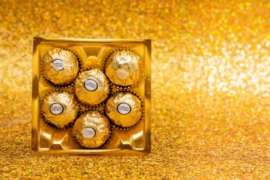 Beyaz etiketli bir kutu Ferrero Rocher çikolatası. Şekerler kare bir kutuda ve sıraya dizildi. Altın arkaplanda şekerler.