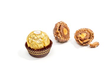 Bir Ferrero Rocher çikolatalı şekeri ve bir kesik beyaz arka planda yatıyor. Altın ambalajlı çikolata kaplı bir fındık beyaz bir arka planda yatıyor..