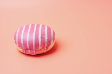 Üzerinde beyaz çizgili pembe ve beyaz bir çörek. Çörek pembe bir arka planda duruyor.