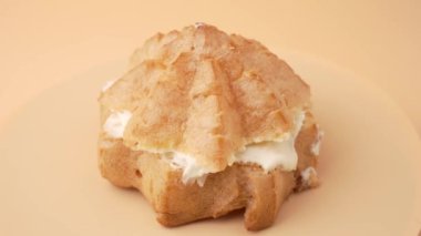 Turuncu arka planda beyaz dolgulu bir hamur işi. Hamur işi yıldız şeklinde ve hafif, havadar bir dokusu var. Beyaz dolgu, altın kabukla çelişiyor ve görsel olarak çekici bir tatlı oluşturuyor.