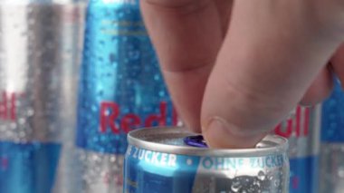 Almanya 6 Ocak 2025. Bir sıra Red Bull konservesi bir tanesi açık olarak gösteriliyor. Kutuların hepsi mavi ve gümüş renginde ve içindeki su damlıyor. Sahne heyecan ve enerjiden oluşur.