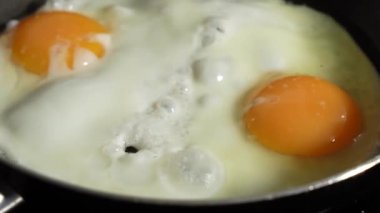 İki yumurtalı tava. Yumurtalar büyük ve turuncu. Kızartma tavası ocakta ve yumurtalar pişiyor..