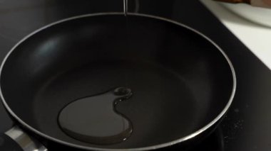 Bir insan tavaya yumurta kırıyor. Yumurta hala kabuğunda. Tava siyah, yumurta sarı.