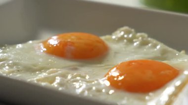 İki yumurta beyaz bir tabakta döner. Yumurtalar portakal beyazı..