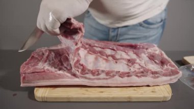 Bir insan, tahta bir kesme tahtasındaki eti kesmek için bıçak kullanıyor. Et, domuz pirzolası gibi görünüyor ve bıçak da onu kesecek açıda duruyor.