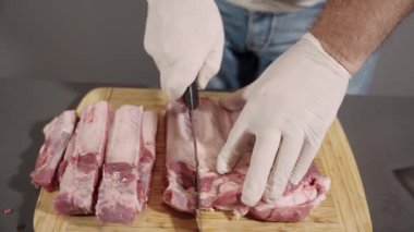 Bir adam et kesme tahtasında et kesiyor. Eldiven takıyor. Et parçalara ayrılmış.