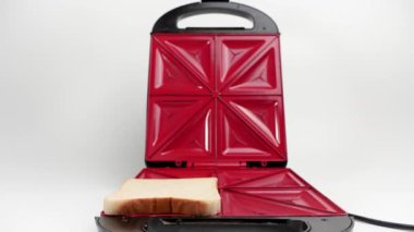 Sandviç yapmak için elektrikli sandviç makinesine ekmek koyar. Beyaz arkaplanda elektrikli sandviç makinesi.