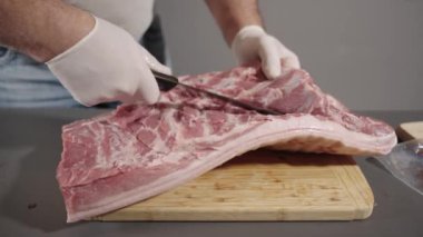 Bir adam bir et parçasını kesme tahtasıyla kesiyor. Eldiven ve siyah bıçak giyiyor..