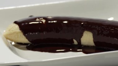 Üstü çikolata kaplı muz. Muz, çikolata kaplı bir tabakta, beyaz arka planda dönüyor..