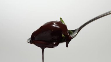 Kaşıktan damlayan çikolatayla kaplı bir kaşıkta çilek. Kaşık gümüş, çikolata kahverengi..