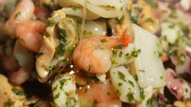 Bir tabak karides, deniz tarağı ve yağlı diğer deniz ürünleri. Karidesler ikiye bölünmüş ve midyeler de ikiye bölünmüş. Yemek maydanozla süslenmiş.