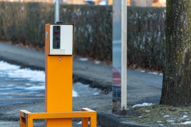 Yolun kenarında bir parkmetre var. Taksimetre turuncu ve üzerinde kırmızı ışık var.