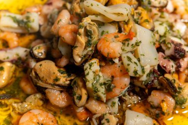 Bir tabakta karides, istiridye ve midye içeren lezzetli bir deniz ürünleri yemeği servis edilir. Karidesler midyelerin ve deniz taraklarının üzerine yerleştiriliyor ve görsel olarak çekici bir sunum yaratıyor.