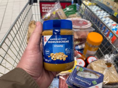 19 Şubat 2025 'te Almanya' da bir kişi bir kavanoz Amerikan stil kremi tutuyor. Kavanoz mavi ve üzerinde etiket var.
