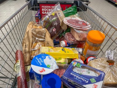 Almanya Berlin 19 Şubat 2025 Ekmek, et ve peynir içeren yiyecek dolu bir alışveriş arabası. Araba plastik torbalar ve konteynırlarla dolu.