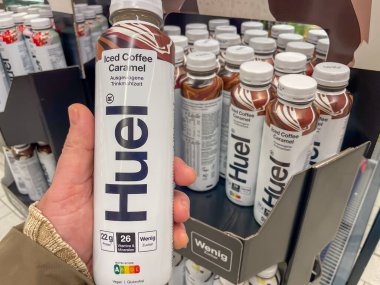 Almanya Berlin 3 Mart 2025 Bir kişi bir şişe Huel tutuyor. Sergide bir sürü Huel şişesi var.