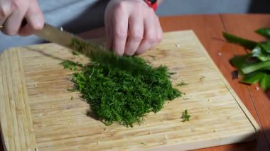 Bir adam ahşap bir kesme tahtasıyla dereotu kesiyor. Dereotu küçük parçalara ayrılmış..