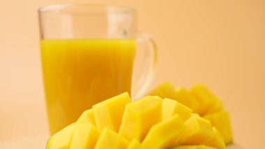 Bir bardak meyve suyu mango dilimlerinin yanında. Meyve suyu sarı ve mango dilimleri de sarı.