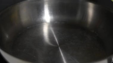 Bir şişe yağ bir tavaya dökülüyor. Tavada gümüş bir leke var.
