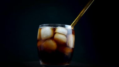 Siyah arka planda buz ve cam tüp ile dönen bir soda bardağı. Buzlu ve gazozlu cam yakın plan..