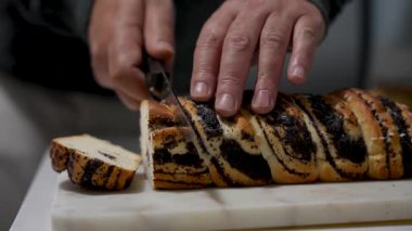 Bir adam haşhaşlı kek kesiyor. Haşhaş tohumlu kek ikiye bölündü. Bıçak ekmeğin sol tarafında..