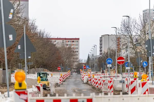 Yol tamiri. Turuncu ve beyaz barikatları ve kırmızı ve beyaz işareti olan bir cadde. Ayrıca sarı ve kırmızı trafik ışıkları da var..