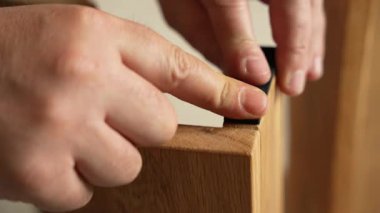 Adamın biri bir tahta parçasına bant yapıştırıyor. Bant siyah ve tahtaya yapışmış. Mobilya kurulumu.
