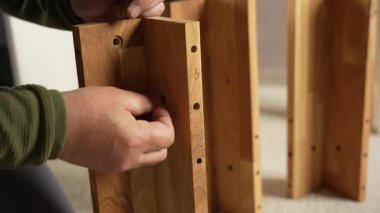Bir adam elinde bir vida tutuyor ve bir tahtaya vida takıyor. Mobilya montajı yapıyor..